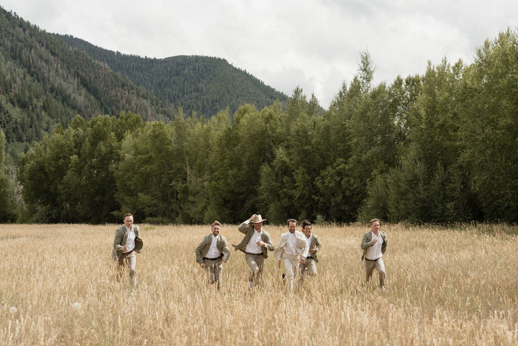 Groom runs through a field with his groomsmen in Aspen, Colorado