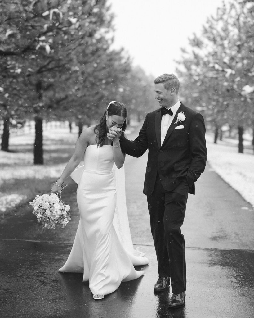 Black and white photo of bride and groom laughing together in falling snow