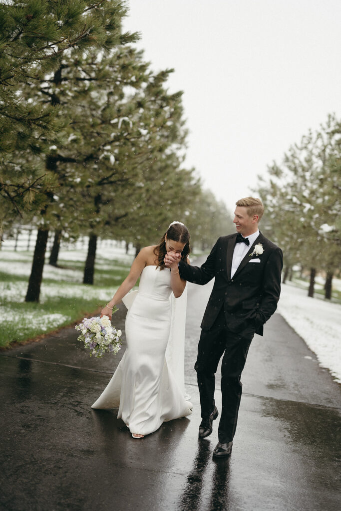 Bride and groom walking hand in hand on snowy road during Colorado winter wedding