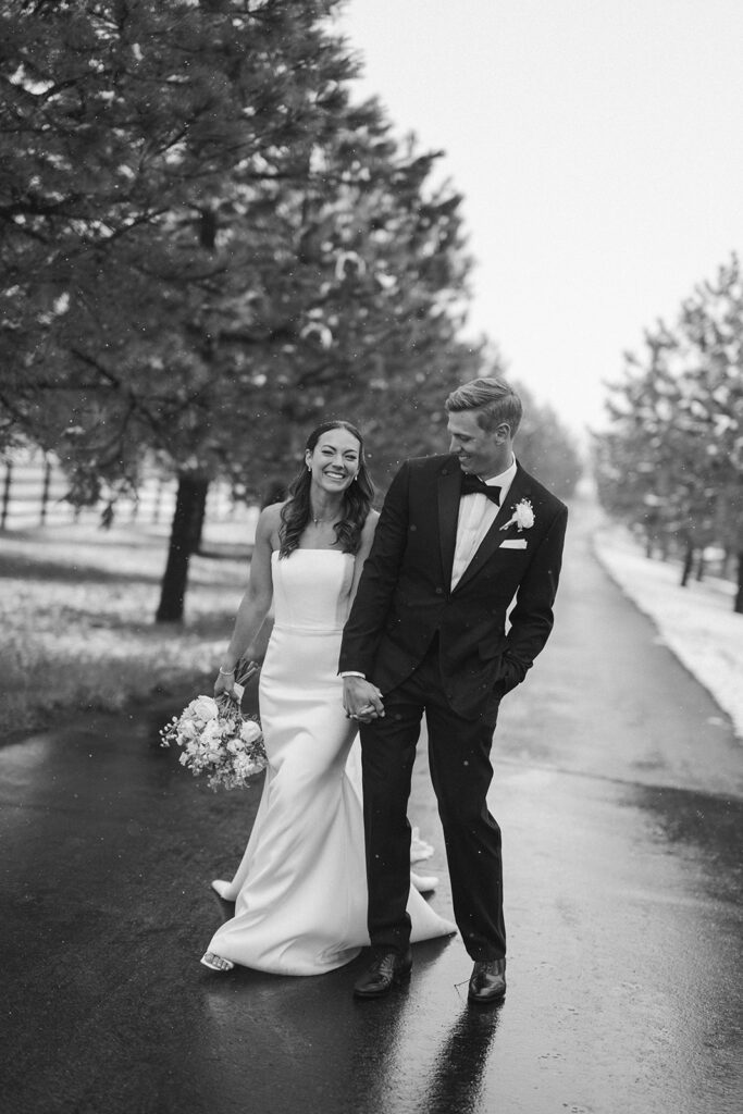 Black and white photo of bride and groom laughing together in falling snow