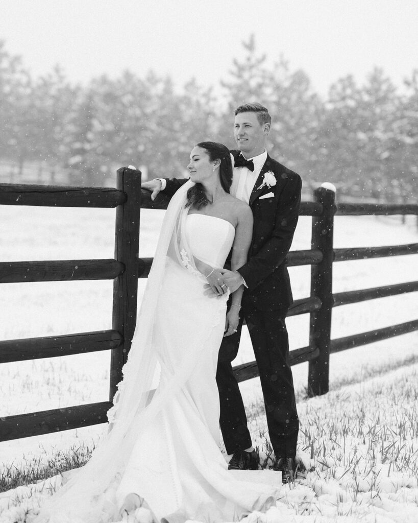 Black and white portrait of couple embracing along snowy fence line