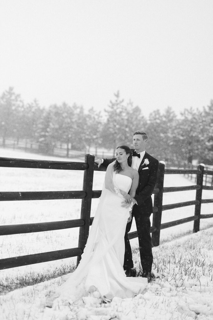 Black and white portrait of couple embracing along snowy fence line