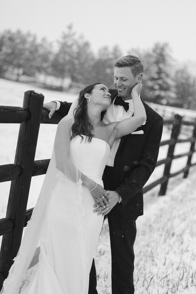 Black and white portrait of couple embracing along snowy fence line