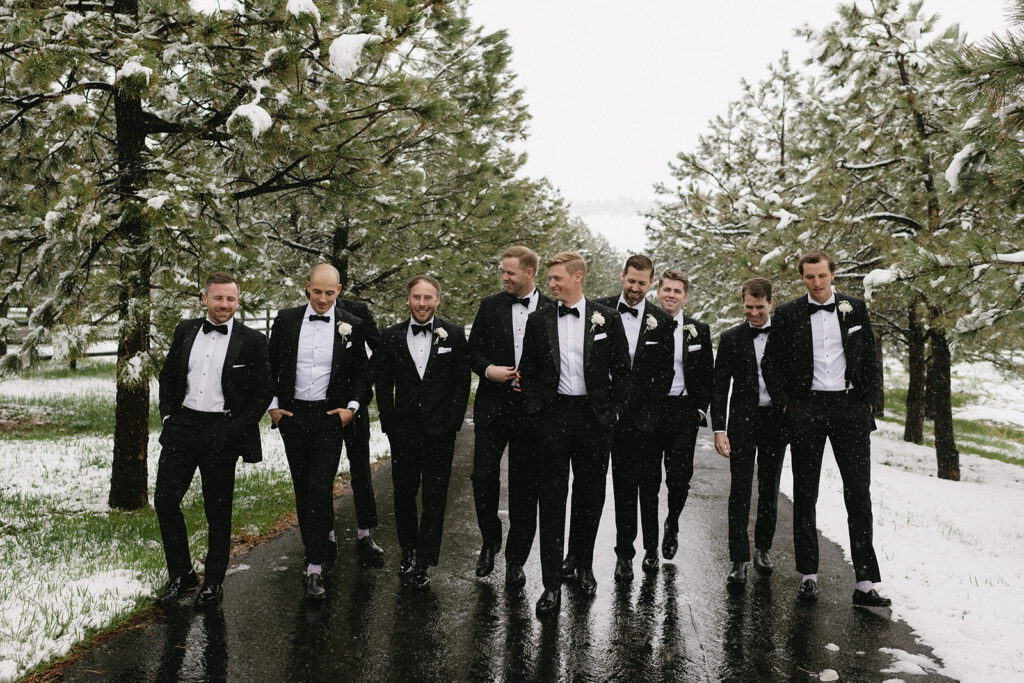 Groomsmen walking together in tuxedos during snowy outdoor wedding
