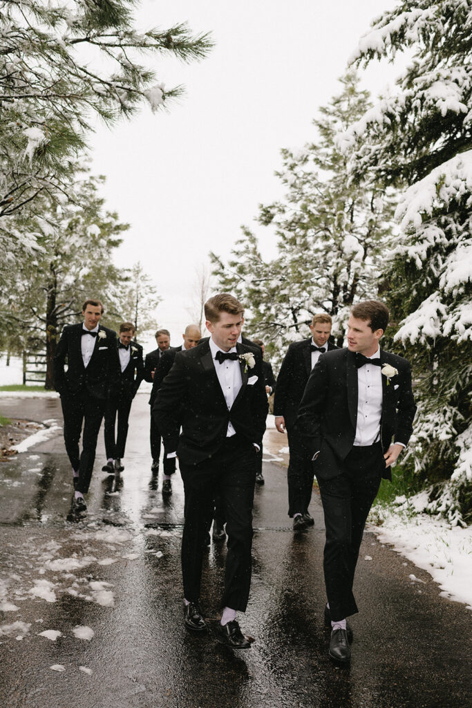 Groomsmen walking together in tuxedos during snowy outdoor wedding