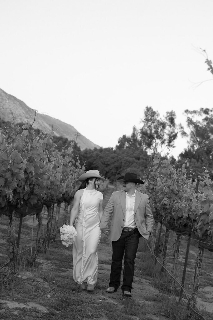 Bride and groom walking in a California vineyard at Rancho Guejito in western wedding attire
